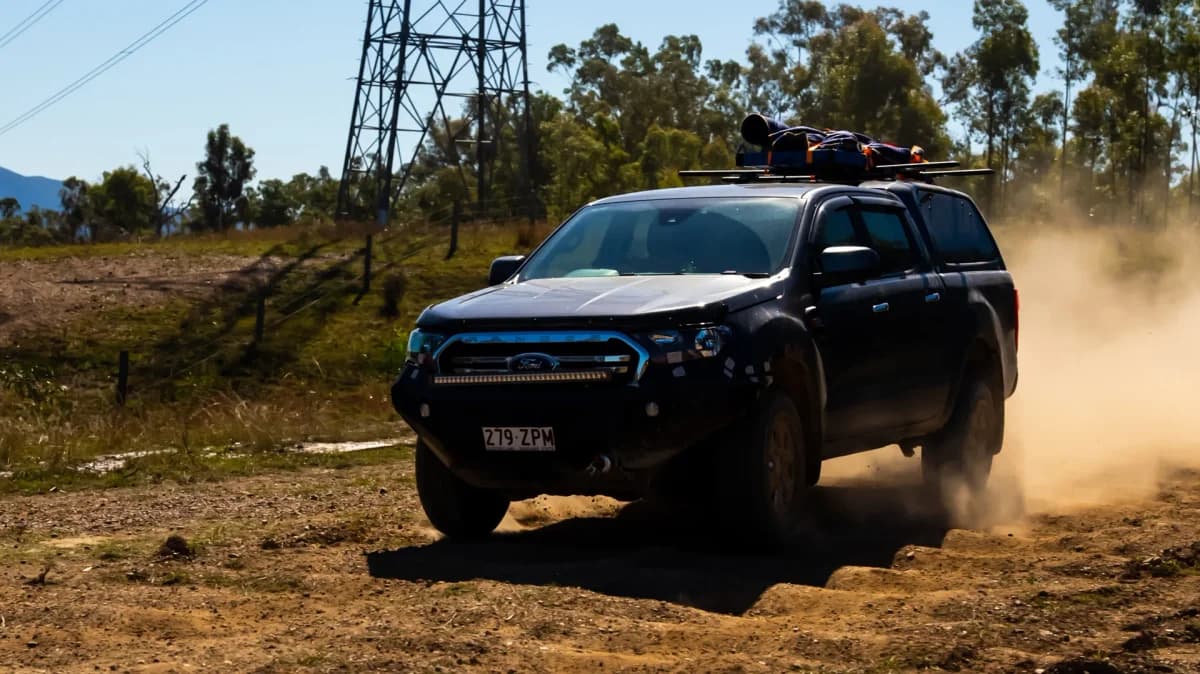 Rear view of a dark ute driving on a muddy trail with EGR dust defenders fitted